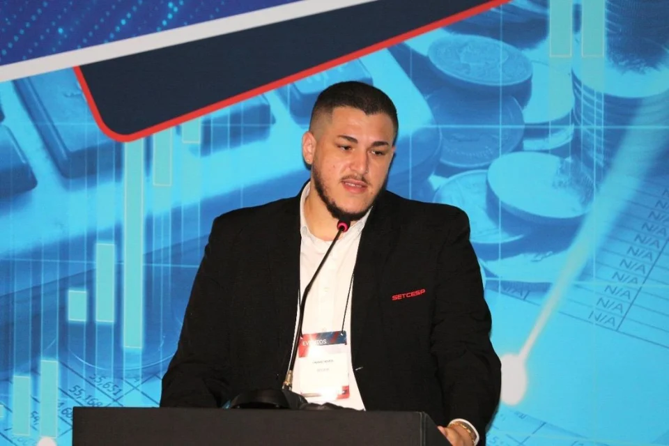 Caique Neves Melo palestrando em evento do setor, com crachá do SETCESP